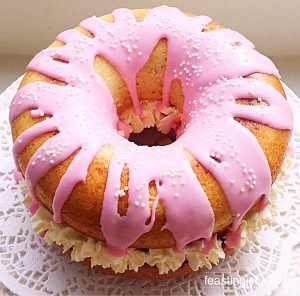 Raspberry And Cream Baked Giant Doughnut with pink drizzle icing a small white sugar ball decorations.