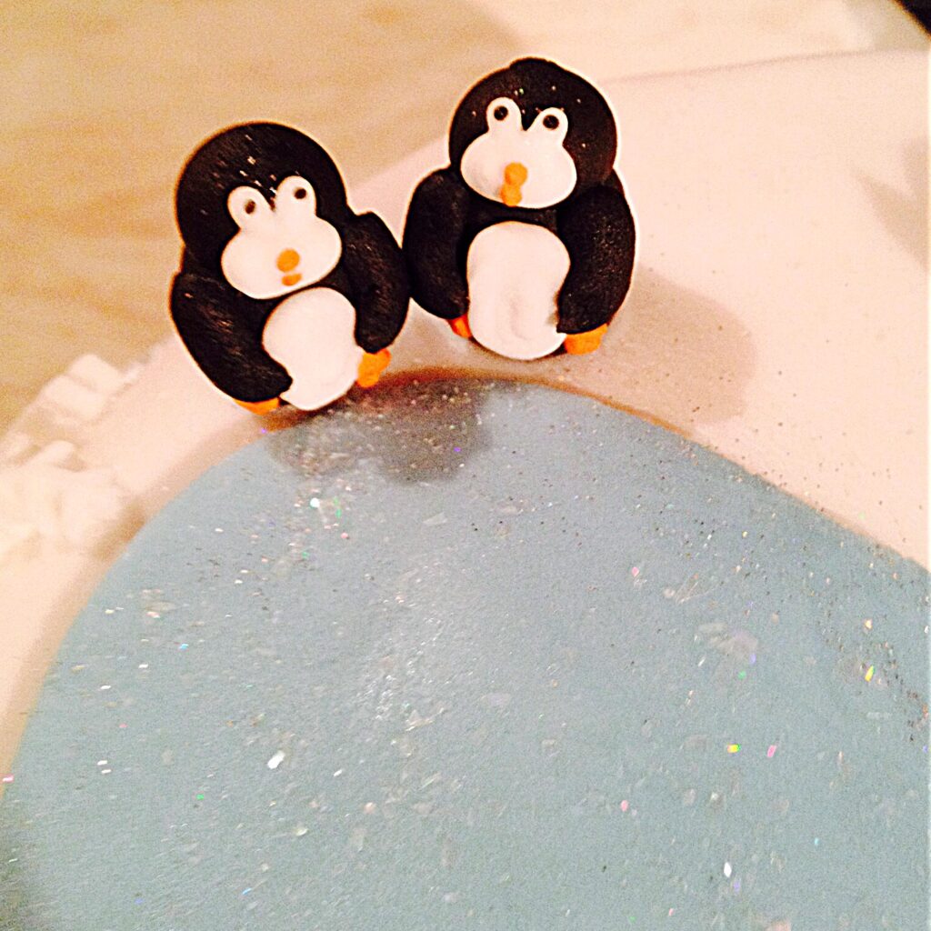 Sugar penguins standing together on top of a fondant covered Christmas cake.