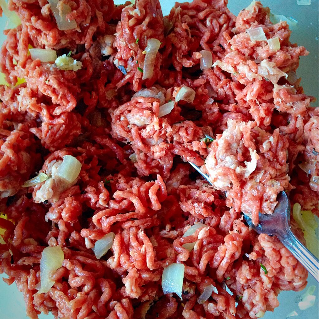 Mixing beef and pork mince together with a fork for light meatballs.
