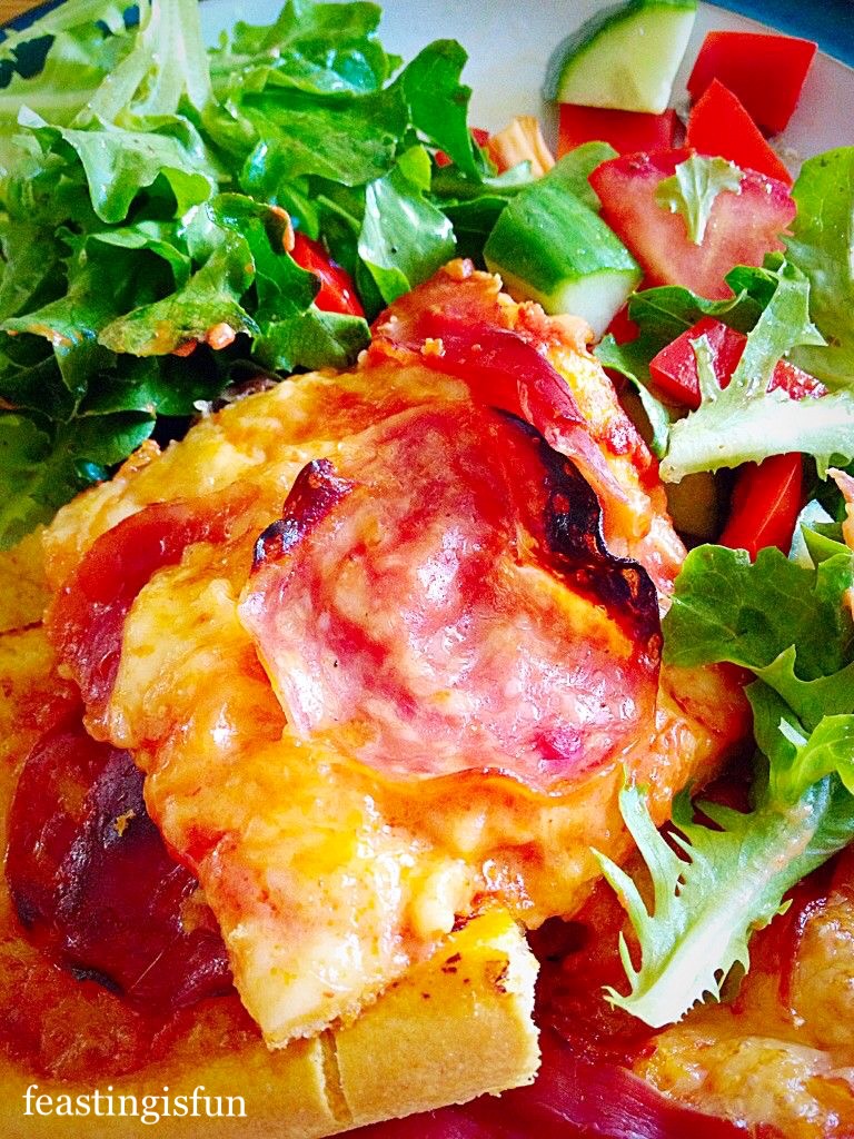 Baked italian bread with cheese and meat topping served as a meal with mixed salad on a plate.