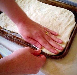 Work with the dough, gradually patting/stretching so that it reaches the edges of the baking tray.