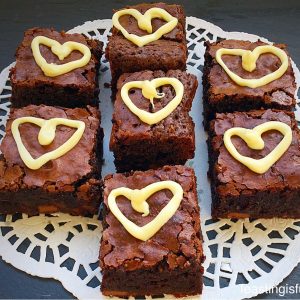 Chocolate fudge brownie bites with white chocolate hearts piped on top.