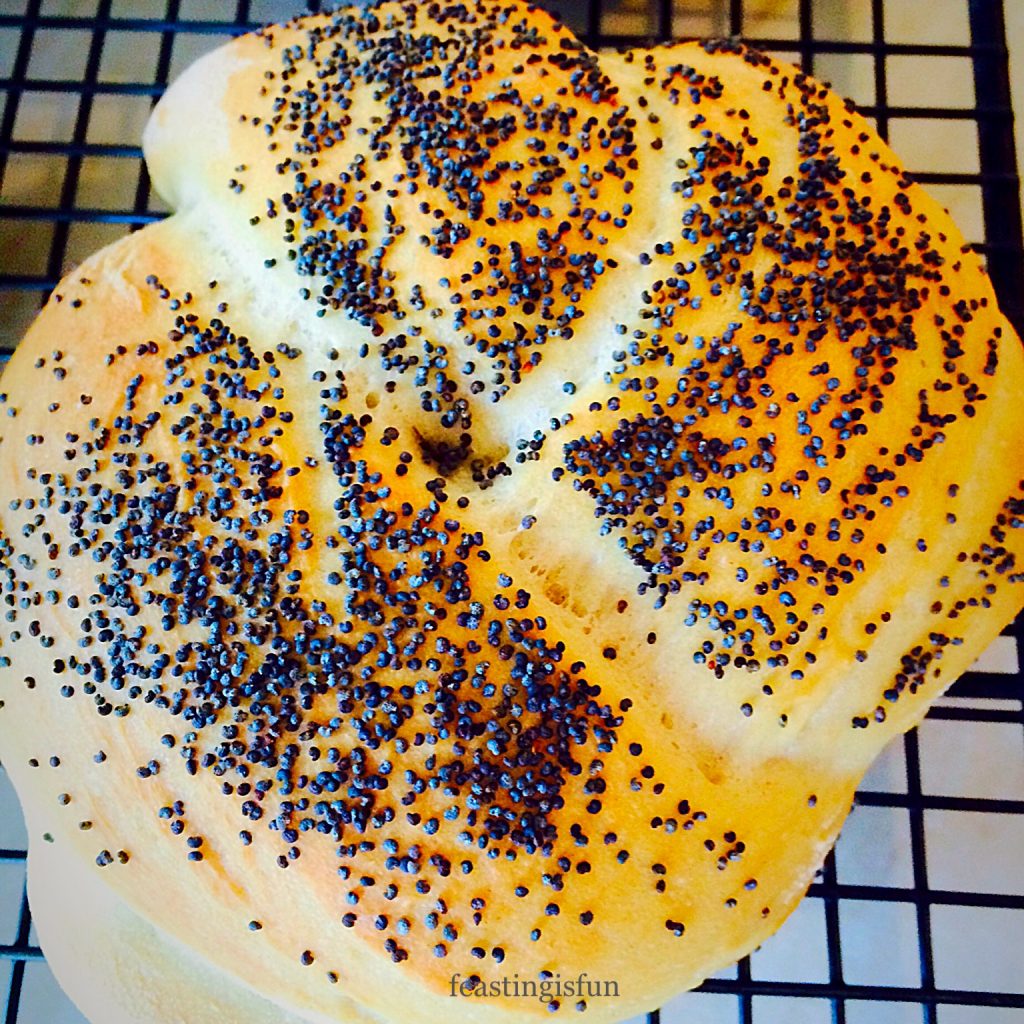 A single knotted poppyseed roll cooling on a rack.