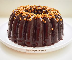 A chocolate Bundt Cake covered in chocolate ganache and topped with pieces of crunchy caramel.