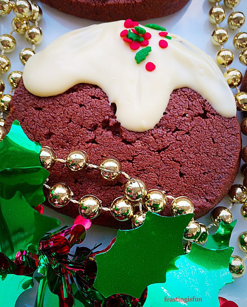 A single Christmas chocolate pudding cookie surrounded by sparkling festive decorations.