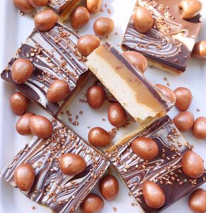 Mini egg millionaires shortbread squares displayed on a white platter showing the different layers.