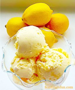 Scoops of lemon ripple ice cream in a fluted glass dessert bowl with fresh lemons in the background.