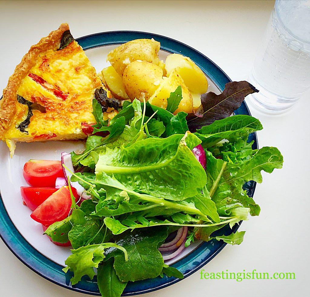 A dinner serving of quiche on a plate with new potatoes and salad.