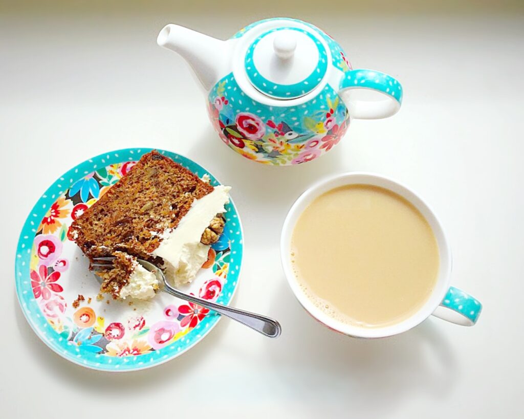 A blue floral tea set with a cup of tea and slice of cake.