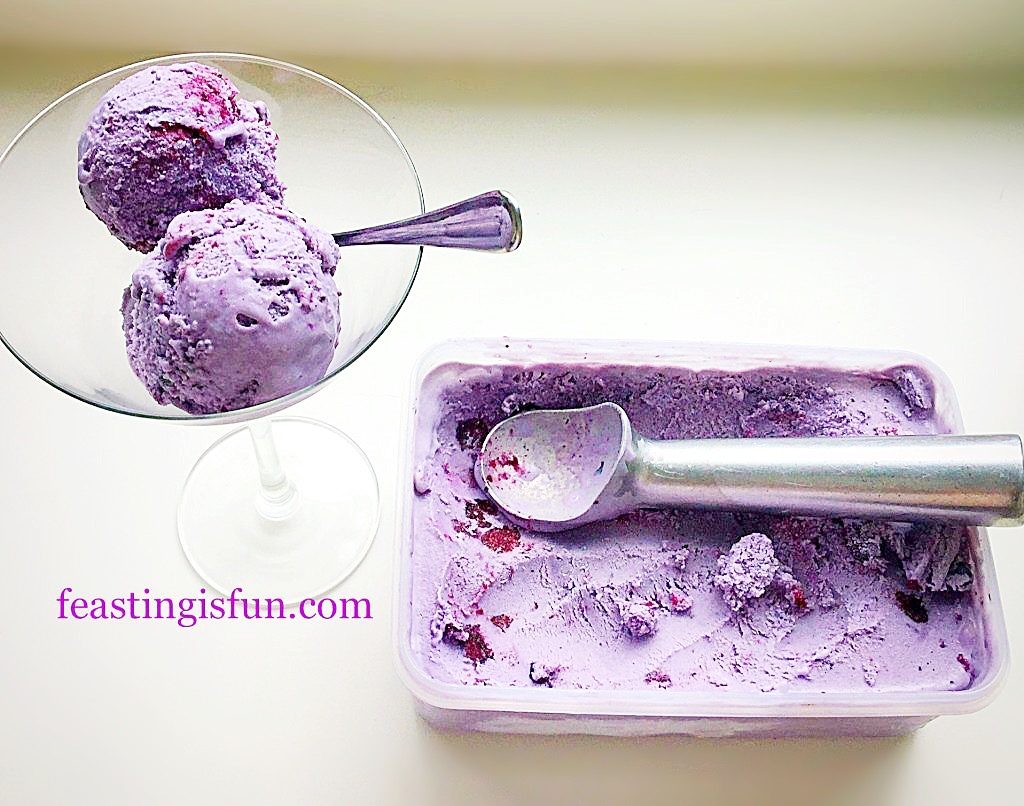 A tub of purple frozen fruit dessert with a martini glass to the side containing scoops of the dessert.