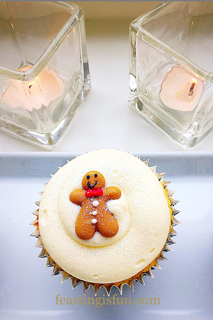 A single small, spiced, festive individual cake with two candles alight behind it.