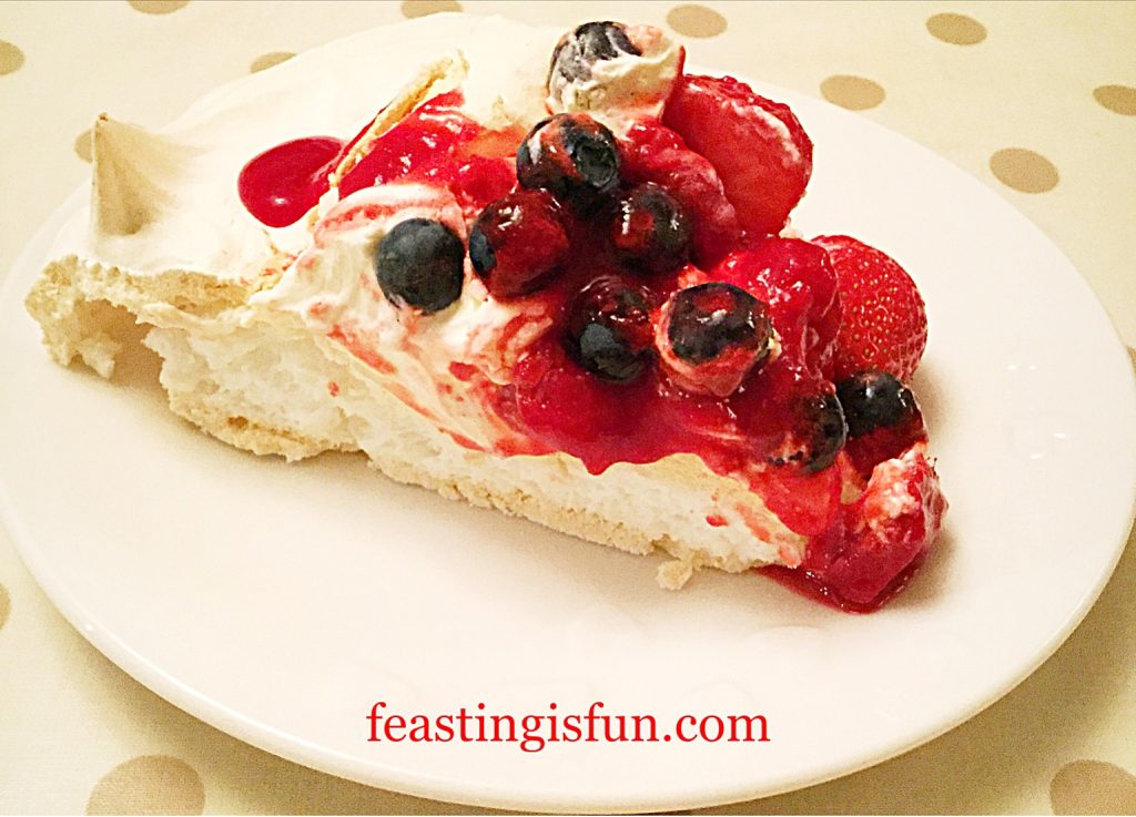 A slice of whipped cream filled meringue topped with fresh berries and a fruit sauce.