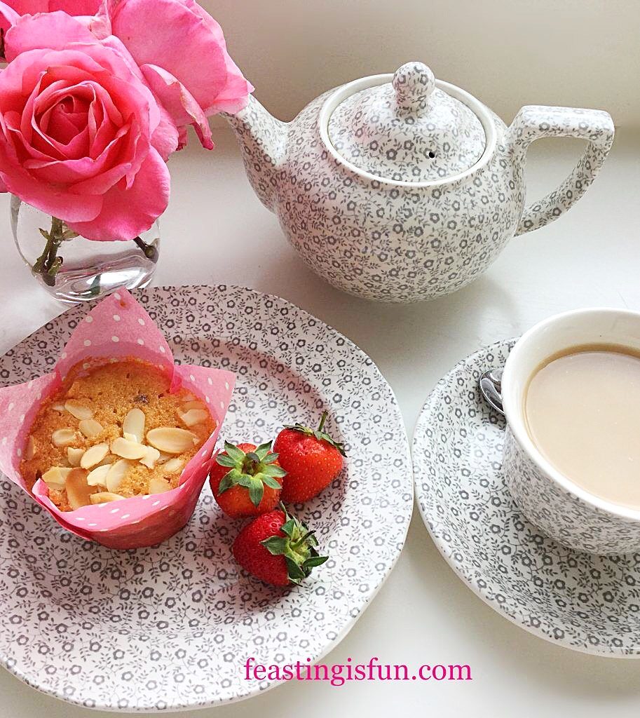 Teapot, cup of tea, muffin on a plate and pink roses in a small vase.