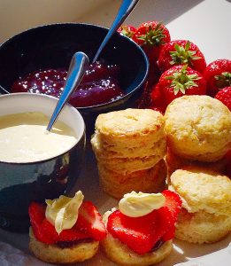 A platter set with small plain scones, fresh strawberries and clotted cream and jam in bowls.