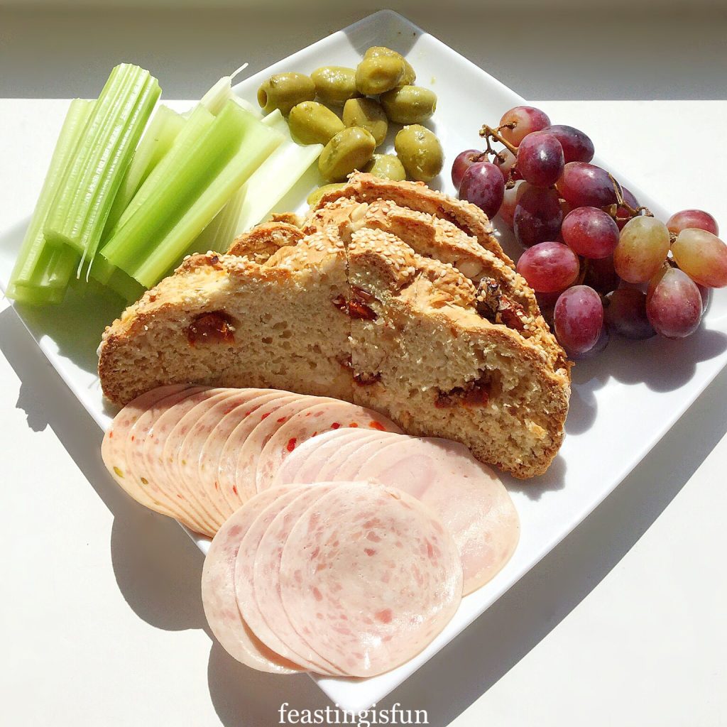 Summer lunch platter with bread, olives, red grapes, celery and a selection of cooked meats.