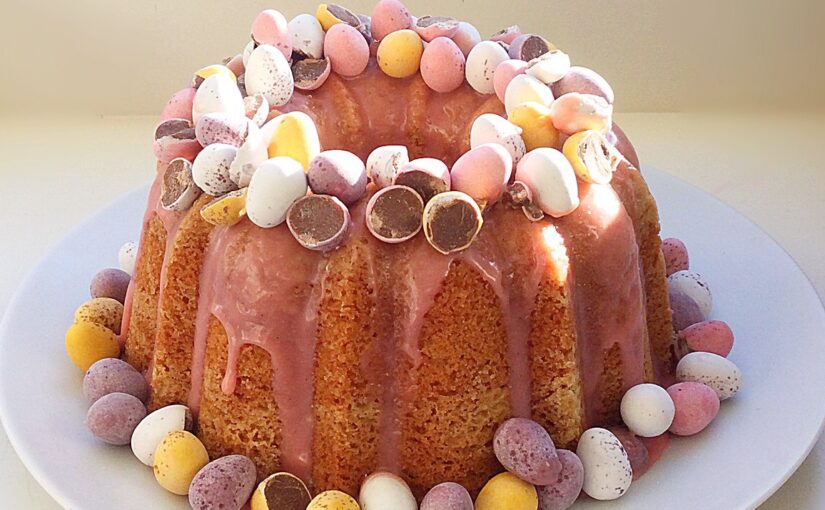 Vanilla sponge Bundt cake with pink coloured chocolate drizzle, topped with mini eggs.