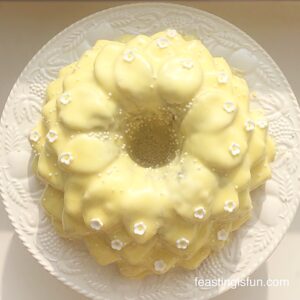 Lemon blueberry Bundt cake covered in a yellow lemon glaze and decorated with white flowers.