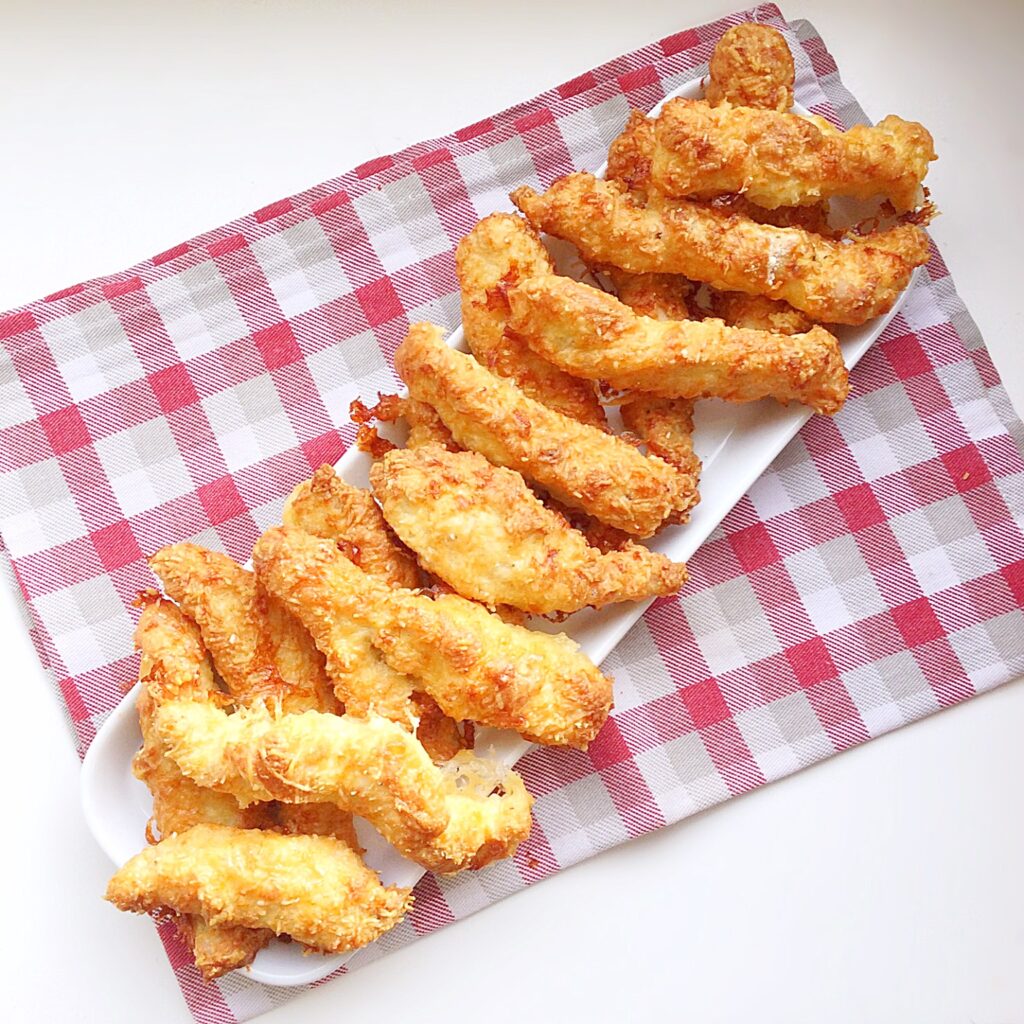 Golden, baked, Parmesan cheese coated strips of chicken on a white platter.